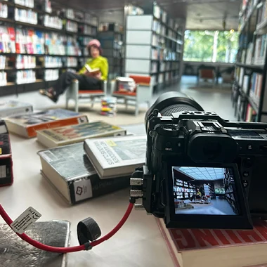 Close-up van een camera op een tafel vol boeken, met een fotoshoot in een bibliotheek op het scherm.