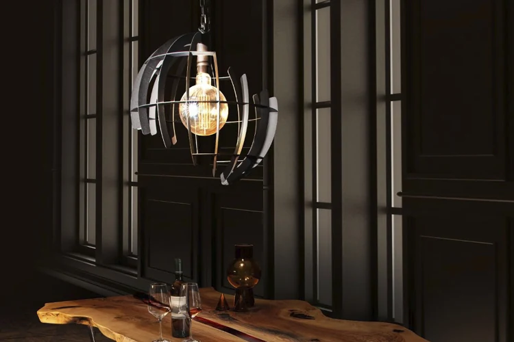 Moderne hanglamp met een open metalen design en een zichtbare gloeilamp, verlicht boven een robuuste houten tafel in een sfeervol donker interieur.